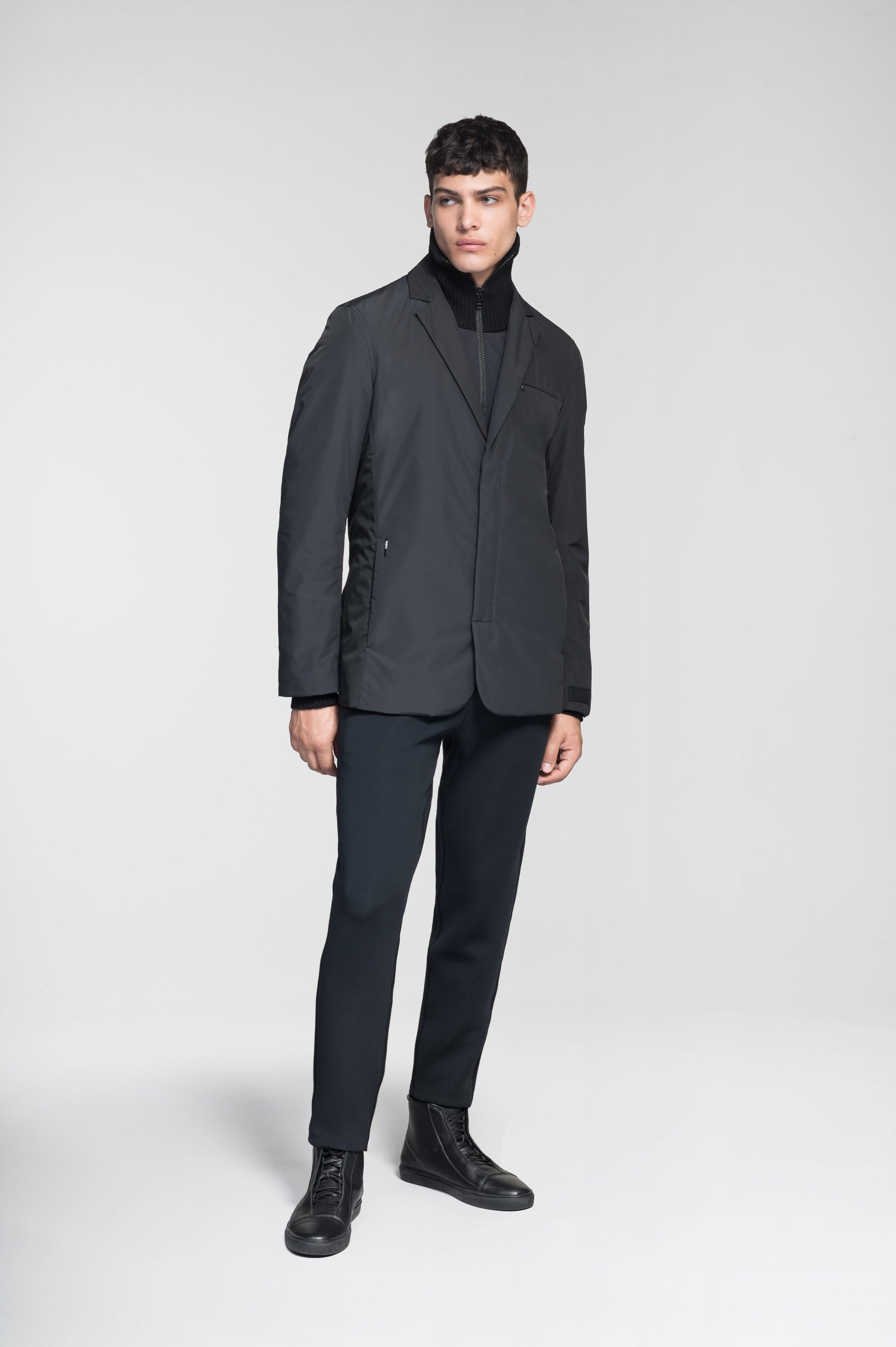 Cody Men's Tailored Travel Blazer in 3-ply micro denier and stretch nylon fabrication with DWR coating, Primaloft Gold Insulation Active+, hidden two-way zipper at centre front with snap closure placket, three invisible exterior zipper pockets, double back pleats, and hidden snap placket at cuffs, in Black