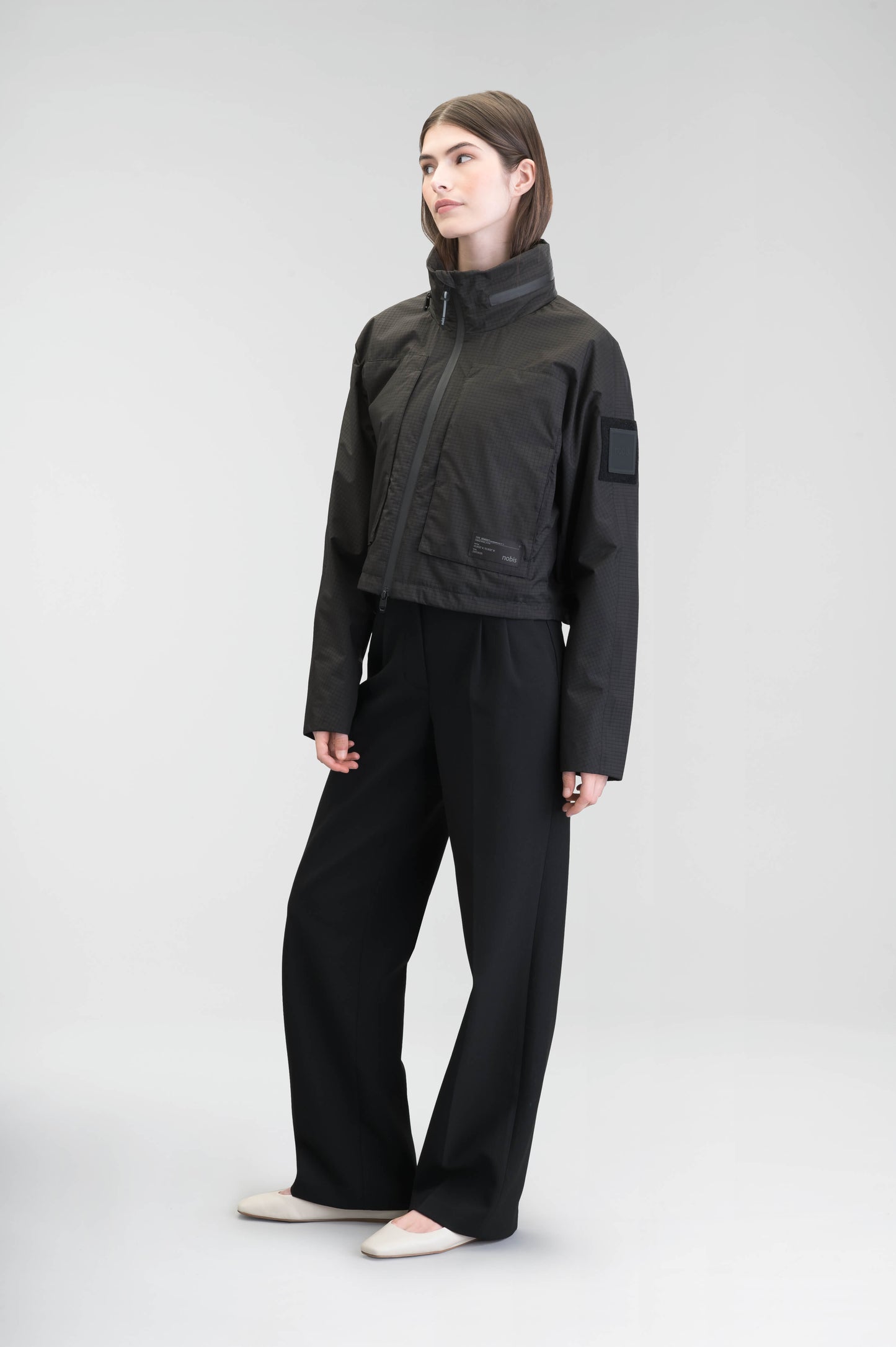 Epsie Women's Cropped Rain Jacket in Black crafted from premium recycled polyester ripstop with a DWR coating and taffeta nylon lining. Features a hidden packaway hood stored in the collar, two-way waterproof front zipper, seam-sealed construction, underarm zip ventilation, adjustable drawcord hem, zippered waist patch pockets, and an interior chest pocket for secure storage. Machine washable. Designed in Canada.