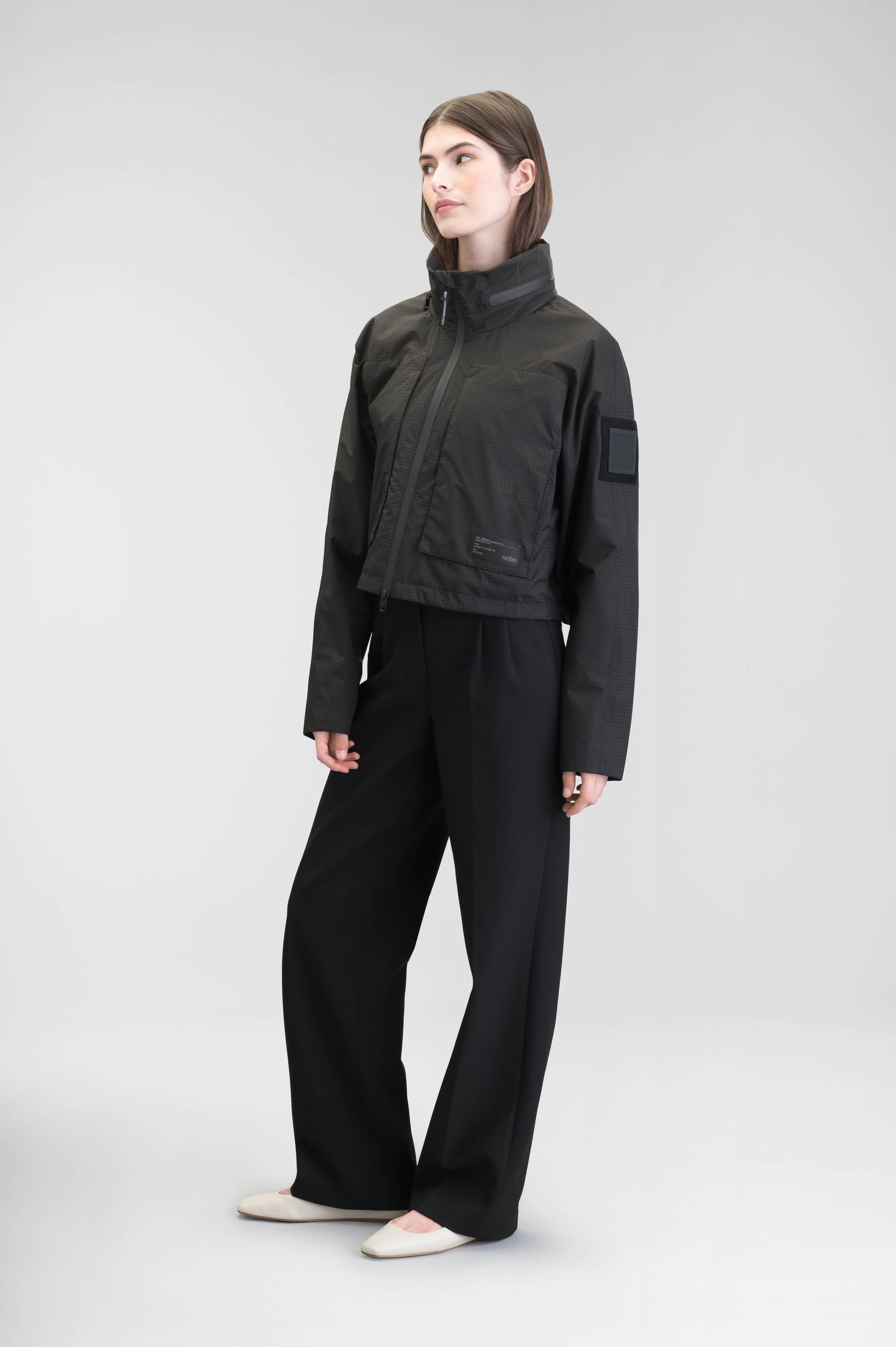 Epsie Women's Cropped Rain Jacket in Black crafted from premium recycled polyester ripstop with a DWR coating and taffeta nylon lining. Features a hidden packaway hood stored in the collar, two-way waterproof front zipper, seam-sealed construction, underarm zip ventilation, adjustable drawcord hem, zippered waist patch pockets, and an interior chest pocket for secure storage. Machine washable. Designed in Canada.