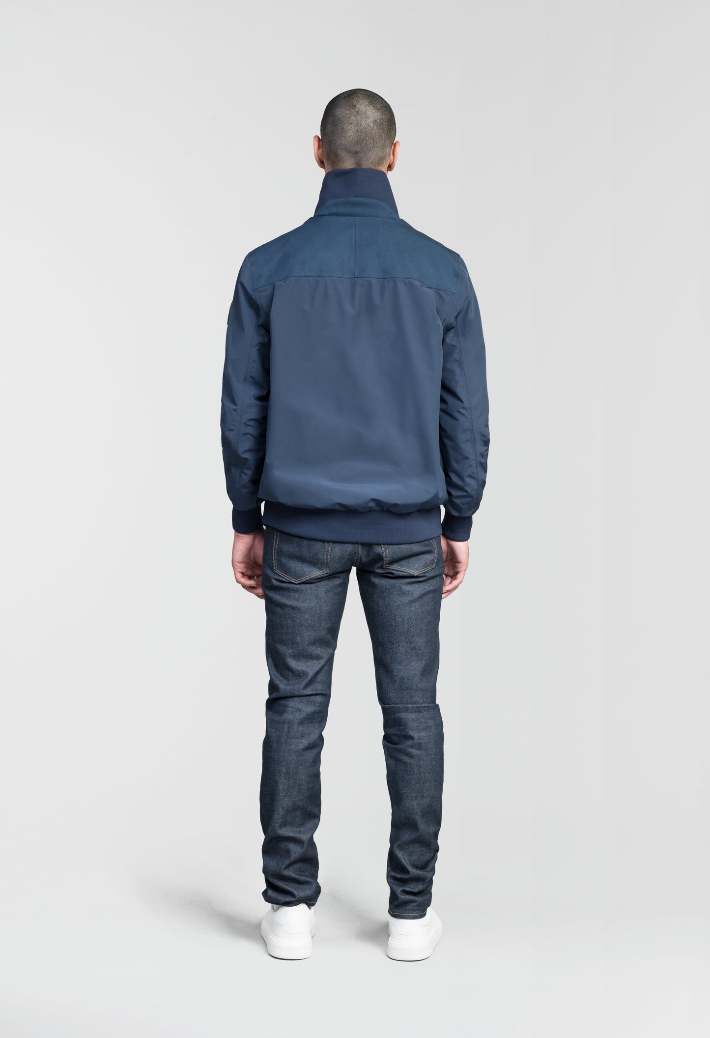 Flint Men's Tailored Rib Collar Jacket in hip length, premium 3-ply Micro Denier fabrication, premium 4-way stretch, water resistant Primaloft Gold Insulation Active +, flap pockets with magnetic closure at waist, side entry pockets at waist, ribbed sleeve cuffs, two-way branded zipper at centre front, box pleat detailing at centre back, large interior zipper pocket, and interior button pocket at left chest, in Marine