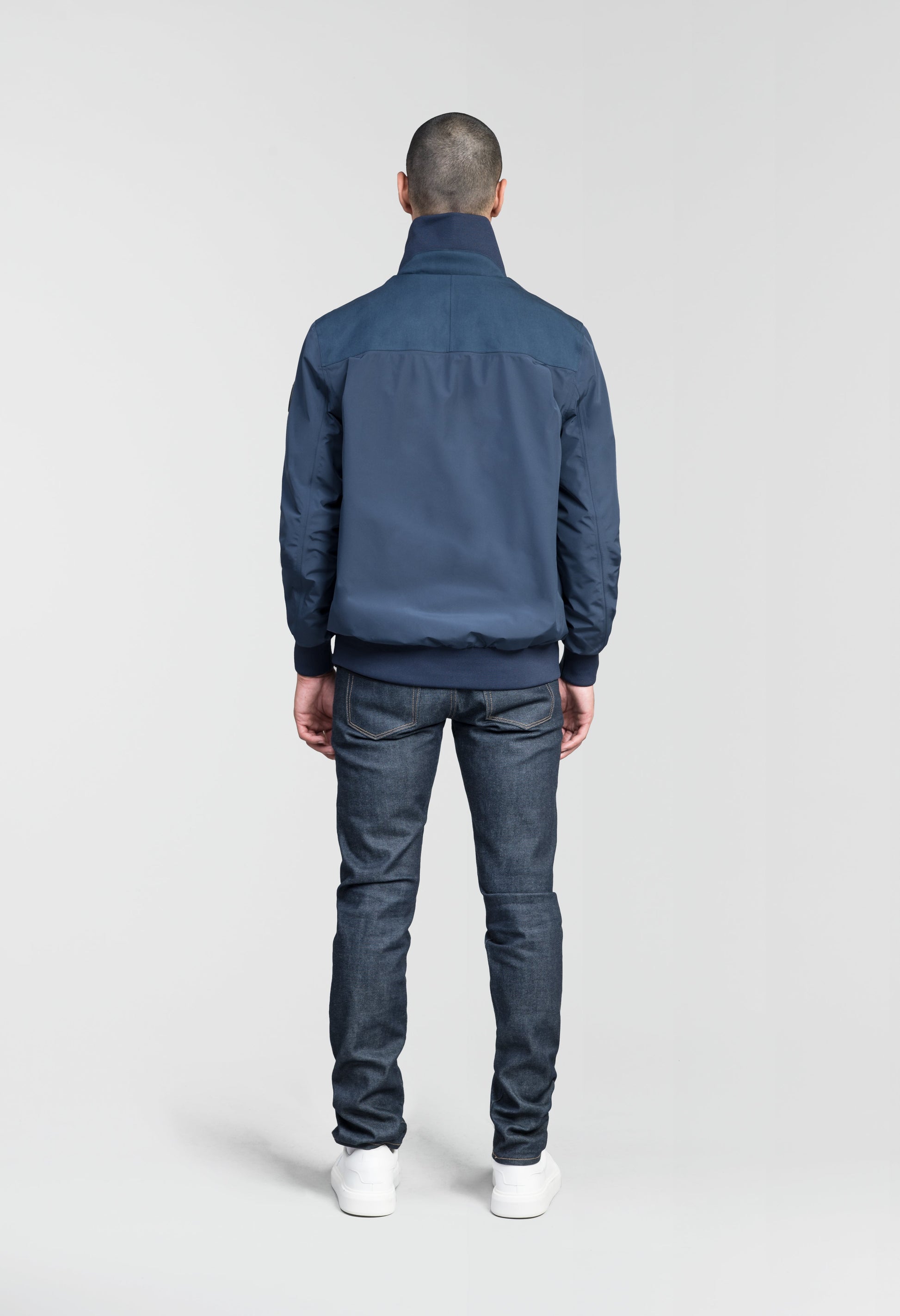 Flint Men's Tailored Rib Collar Jacket in hip length, premium 3-ply Micro Denier fabrication, premium 4-way stretch, water resistant Primaloft Gold Insulation Active +, flap pockets with magnetic closure at waist, side entry pockets at waist, ribbed sleeve cuffs, two-way branded zipper at centre front, box pleat detailing at centre back, large interior zipper pocket, and interior button pocket at left chest, in Marine