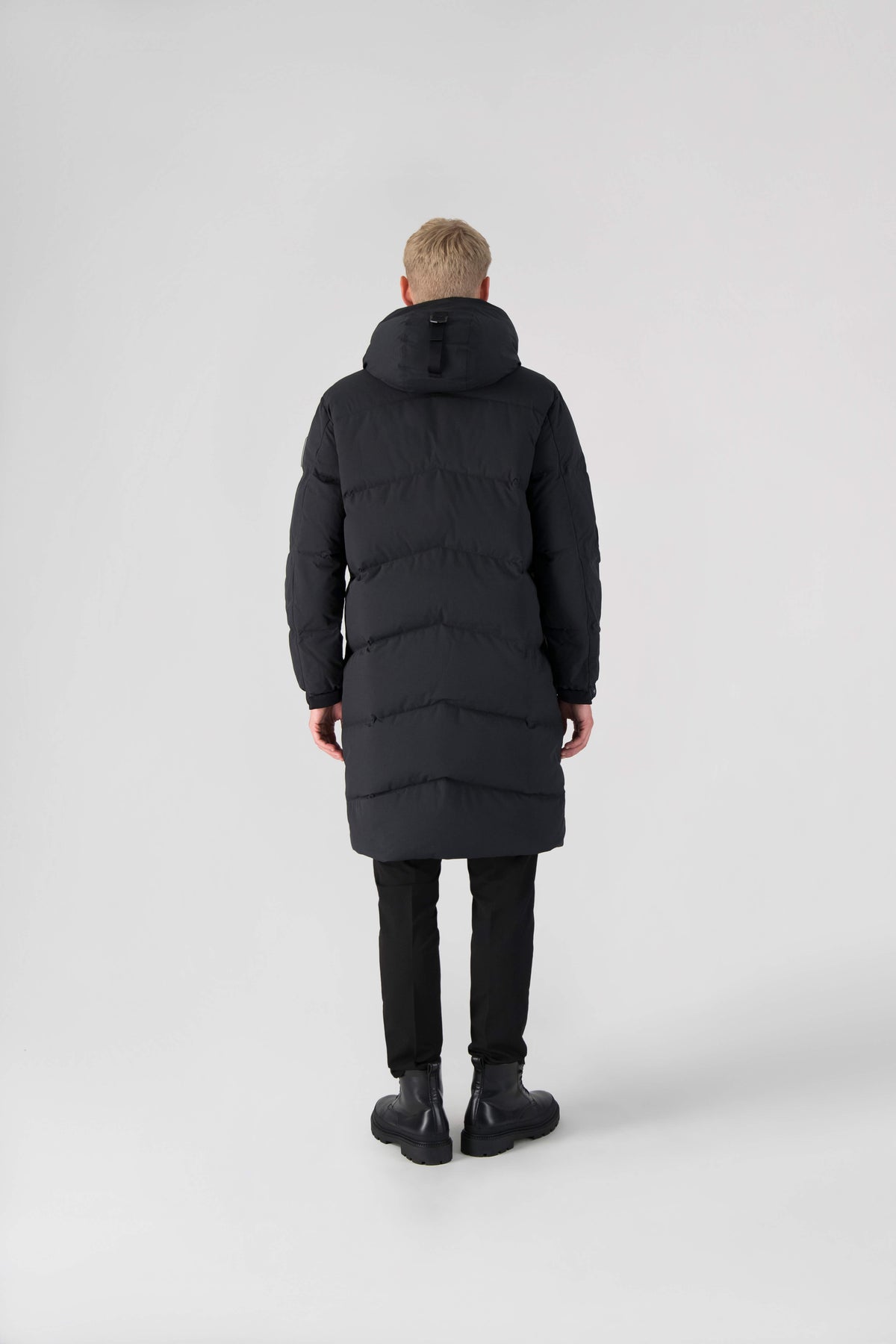 Granger long jacket in Black stretch ripstop fabric with DWR coating, insulated with Canadian white duck down and Primaloft. Features a two-way zipper, magnetic closure, and adjustable cuffs for warmth and weather protection.