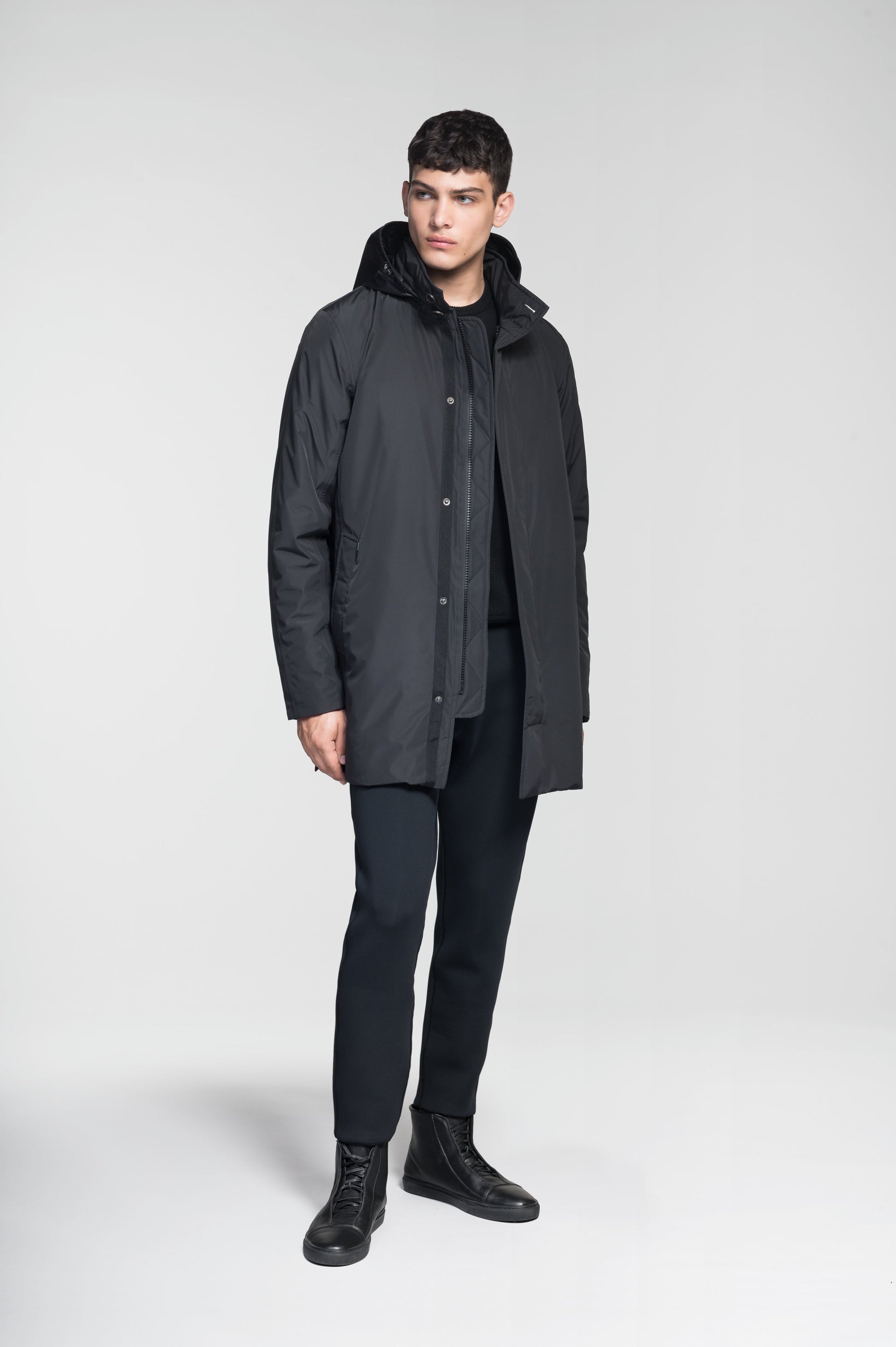 Pike Men's Tailored Mac Coat in thigh length, premium 3-ply Micro Denier fabrication at body and cire technical nylon taffeta fabrication at hood, premium 4-way stretch, water resistant Primaloft Gold Insulation Active+, hidden 2-way zipper with snap closure wind flap, single welt pockets with magnetic closure at waist, hidden snap placket at cuffs, pit zippers for ventilation, interior zipper pocket at right chest, and interior button pocket at left chest, in Black