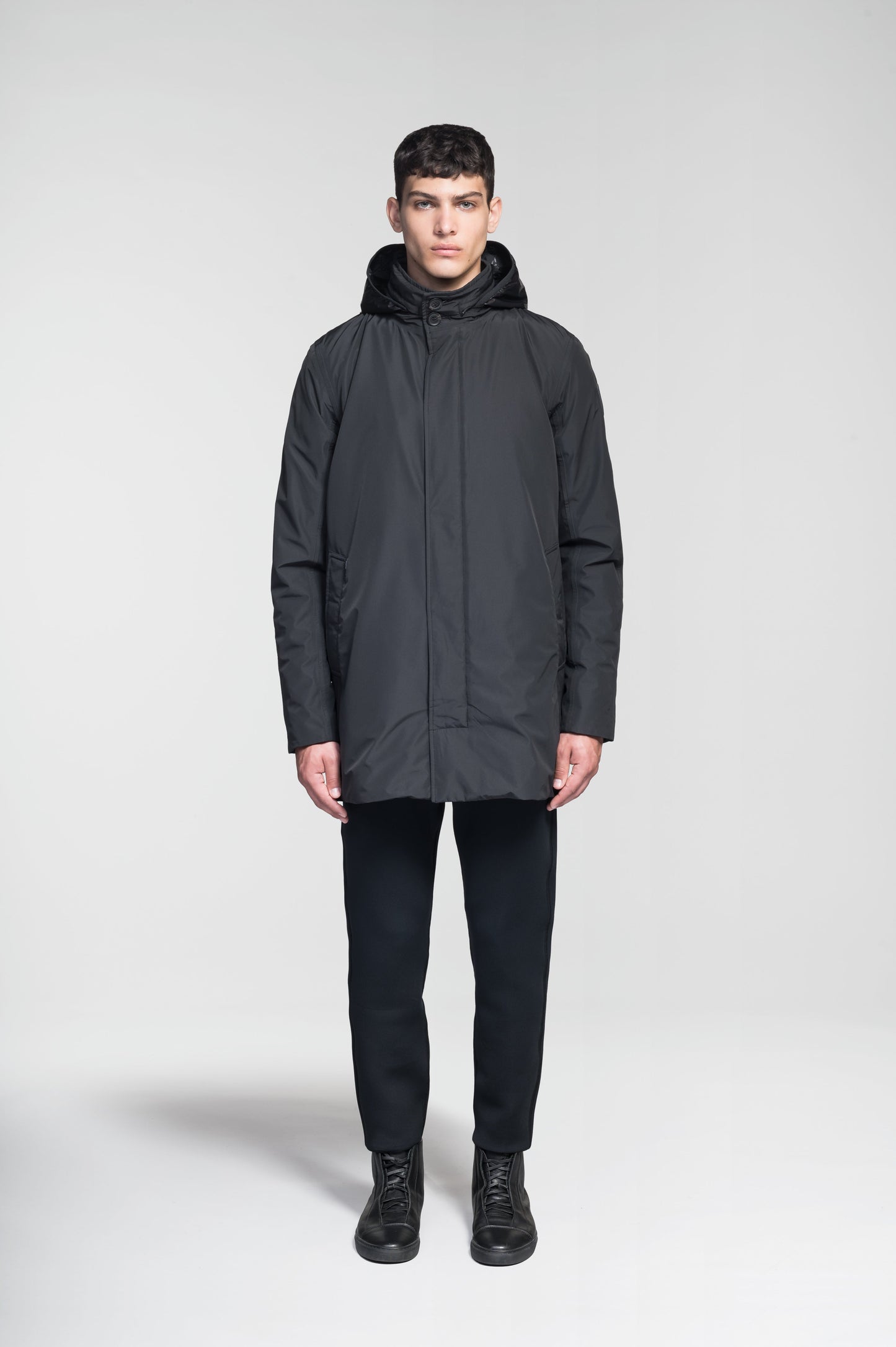 Pike Men's Tailored Mac Coat in thigh length, premium 3-ply Micro Denier fabrication at body and cire technical nylon taffeta fabrication at hood, premium 4-way stretch, water resistant Primaloft Gold Insulation Active+, hidden 2-way zipper with snap closure wind flap, single welt pockets with magnetic closure at waist, hidden snap placket at cuffs, pit zippers for ventilation, interior zipper pocket at right chest, and interior button pocket at left chest, in Black