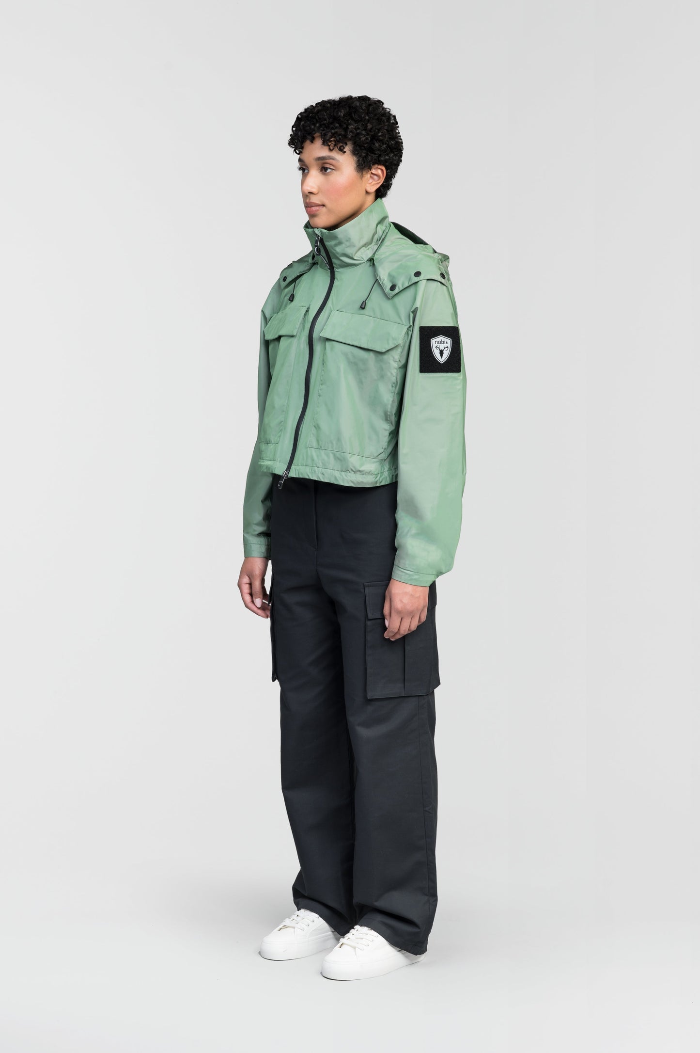 Viva Women's Performance Cropped Jacket in waist length, premium iridescent fabrication, removable hood with peak, adjustable hood draw cords and toggle, 2-way branded zipper at centre front, oversized magnetic closure flap pockets at chest with side entry, interior adjustable draw cord at hem, large interior zipper pocket, and adjustable snap cuffs, in Comfrey